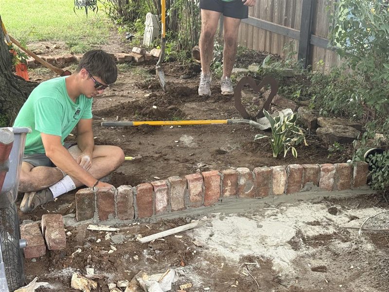 Graf Lawncare crew laying brick edging around a garden bed